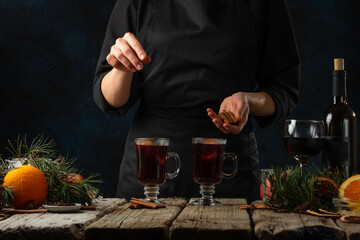 Chef pours cinnamon into glasses with aromatic muled wine with fragrant spices dark background. Concept of preparing hot winter alcoholic drink. Frozen motion. Traditional recipe