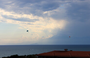 People on parachutes fly over the Mediterranean sea in Turkey on a cloudy summer evening