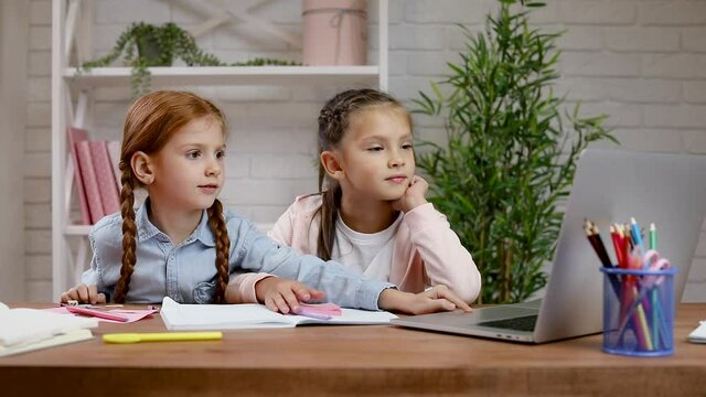 two little children girl using laptop for doing school tasks at home and writing notes. online lesson at home