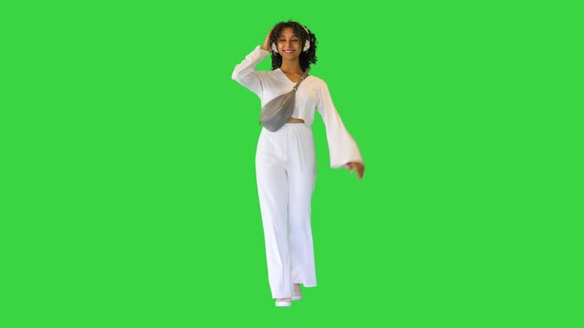 Smiling young african american woman listening to music on headphones while walking on a Green Screen, Chroma Key.