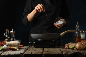 Professional chef pours spices into frying pan for cooking traditional indian curry. Backstage of preparing on dark blue background. Concept of organizing the cooking process. Frozen motion.