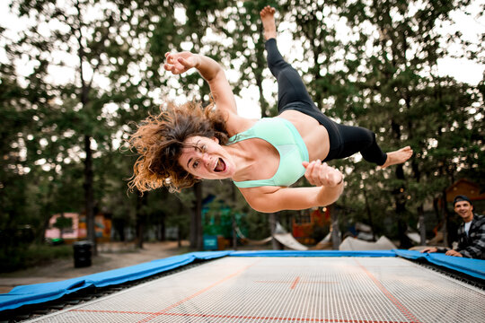 surprised cheerful woman with curly hair actively jumping on trampoline - Powered by Adobe