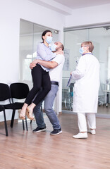 Excited young couple after receiving good from doctor with face mask in hospital waiting area. Positive man and woman in clinic after good test results.