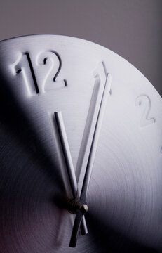 Close up of a clock showing five minutes past twelve. 