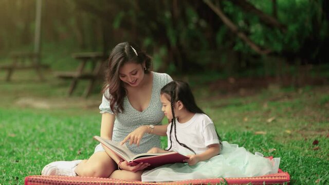 single mother having family time with daughter reading book outdoor