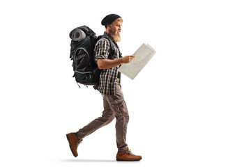 Full length profile shot of a young bearded man with hiking equipment walking and looking at a map