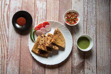 Alu paratha, an Indian delicacy of mashed potatoes in wheat bread in a plate with condiments.