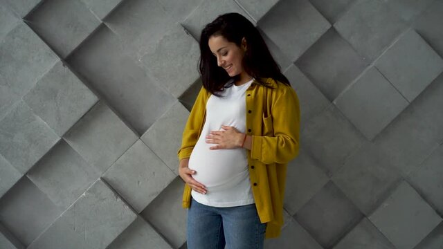 Young happy pregnant woman holding and stroking her belly 