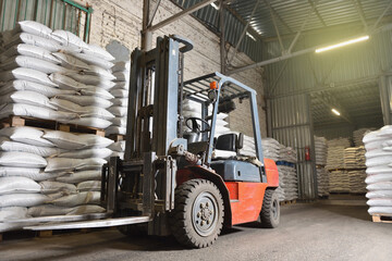 A forklift stands in a warehouse next to pallets with full bags