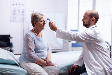Fototapeta premium Measuring old senior woman temperature during consultation in clinic examination room. Medical consultation for infections and disease during global pandemic,flu, tool, sickness.