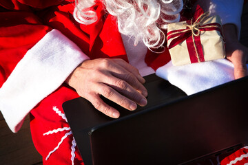 Santa Claus with a laptop and a gift in his hand. Order gifts for Christmas and new year through...