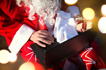 Santa Claus with a laptop and a gift in his hand. Order gifts for Christmas and new year through...