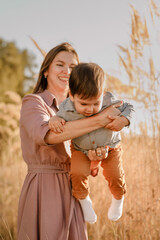 Fototapeta premium Portrait of happy loving mother hugging her baby son in the sunny park near river