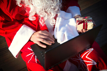 Santa Claus with a laptop and a gift in his hand. Order gifts for Christmas and new year through...