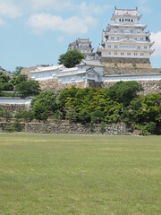 Ancient samurai castle in Himeji city in Japan with white walls, dark tile roofs and stone walls on a sunny day in summer with blue sky and white clouds