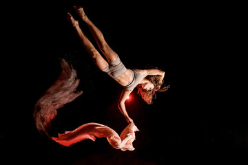 attractive female athlete flying upside down with scarf at dark time