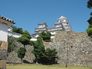 Ancient samurai castle in Himeji city in Japan with white walls, dark tile roofs and stone walls on a sunny day in summer with blue sky and white clouds