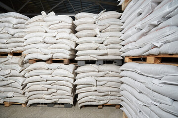 Fototapeta na wymiar Many white full bags with cereals lie on pallets in a warehouse