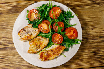 Fried chicken breast with salad of fresh arugula and cherry tomatoes on wooden table. Top view