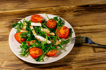 Tasty salad of fried chicken breast, fresh arugula and cherry tomatoes on wooden table