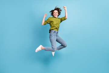 Photo portrait of crazy ecstatic woman jumping up celebrating fists in air isolated on pastel light blue colored background