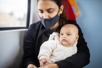 Woman sitting next to a window in a bus and holding her baby in her arms