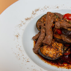 warm salad of eggplant and meat on white plate. beige background. close up