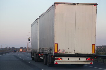 European white van truck with semi trailer drive on empty two lane suburban asphalted highway road, back view at summer evening on clear sky background, transportation delivery logistics