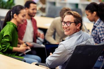 Happy cheerful mature businessman smiling at camera while having brainstorming meeting with...