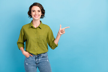 Photo of charming lady short hairstyle look camera direct indicate finger empty space hands pockets wear denim jeans green shirt isolated blue color background