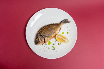 dorado with lemon on white plate. red background. top view. flat lay.