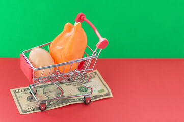A shopping basket on a red and green background with plastic products stands on a banknote. The...