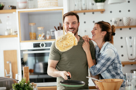 Husband and wife making pancakes at home. Loving couple having fun while cooking.