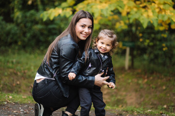 Naklejka na ściany i meble Little girl walking with her mom in forest. Mother with her daughter in leather jackets