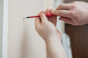 Worker manually tightening an artwork hang screw into a drilled hole in white wall with screwdriver, renovating, decorating and improving home