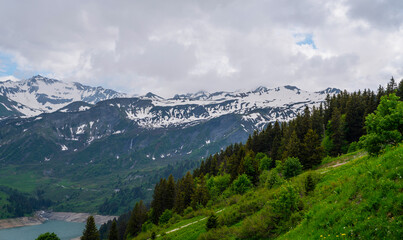 Beautiful view of scenic mountain landscape in the Alps fresh green meadows with blue sky and clouds in spring. Picturesque morning view of Roselend lake, Auvergne-Rhone-Alpes, France, Europe.