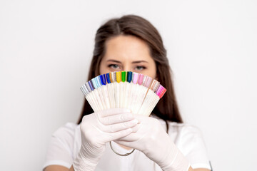 Portrait of female manicure master covering her face with nail sample palette on white background