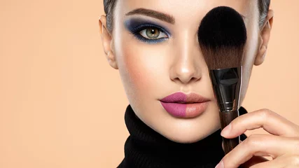 Poster Portrait of a girl with cosmetic brush at face. Woman covering one eye on the face using makeup brush. One half face of a beautiful white woman with  bright makeup and the other is natural. © Valua Vitaly