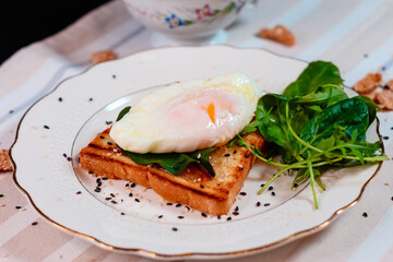 A breakfast with poached egg on toast with green salad leaves.
