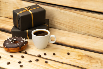 Chocolate donut, a cup of coffee and gifts in black packaging on a wooden background.