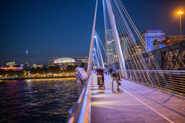 Fototapeta premium Cityscape at night from the handrail of a bridge with pedestrians walking on it