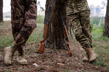 Legs of Hunters Standing Leaning to Tree Rifles.