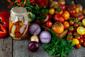 Tomatoes, peppers, onions on the table. Preservation of the autumn harvest of vegetables. Glass jar with pickled tomatoes. Wooden background. Vegetable food. Still life. Tomato of different varieties.