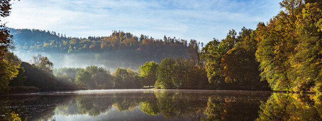 Fototapeta premium Lake fog landscape with Autumn foliage and tree reflections in Styria, Thal, Austria