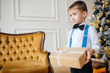 A child in smart clothes stands with a gift box near the New Year tree. Christmas concept