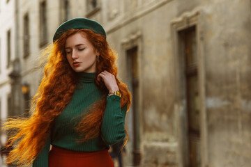 Obraz premium Outdoor autumn fashion portrait of elegant redhead woman with long beautiful curly hair, wearing green beret, turtleneck, walking in street of European city. Copy, empty space for text