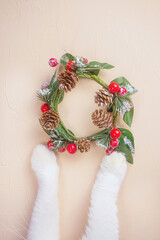 Obraz na płótnie Canvas Cat paws and Christmas wreath on a light background. Cute concept for christmas and new year with pets. Top view, copy space.