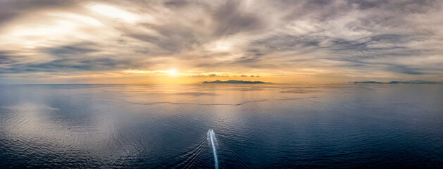 A boat traveling over idyllic, calm ocean towards an lonely island during sunset time with...