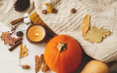 Autumn flat lay. Candle, pumpkins, cozy knitted sweaters, autumn leaves, spices, cotton