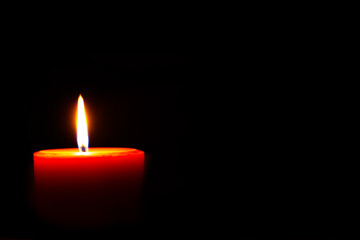Burning red candle against dark background.